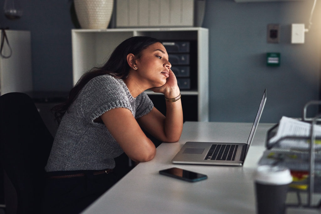 Shot of a young businesswoman looking bored while working on a laptop in an office at night