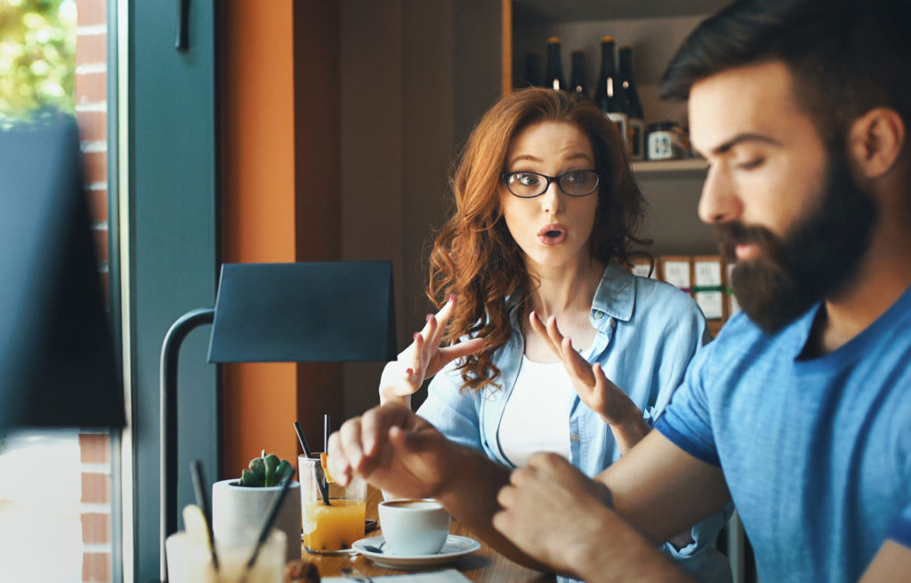 Closeup side view of mid 20's couple having an argument at a coffee place. She's spitting fire because of something he might have done and he's quietly looking down and listening.