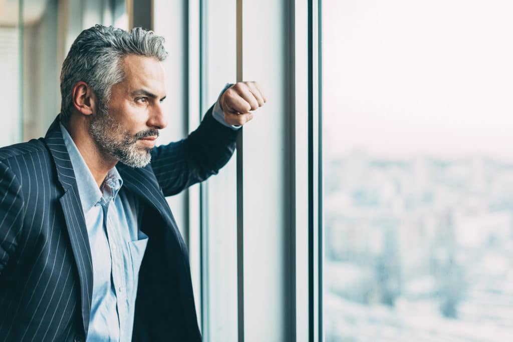 Serious mature businessman looking out of the window, with copy space.